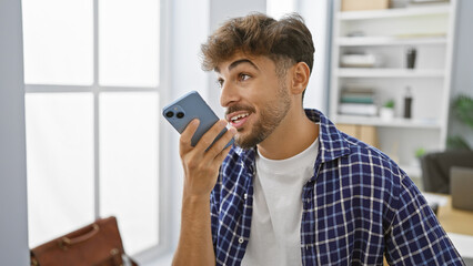 Confident young arabian man smiling while sending voice message on his smartphone in office