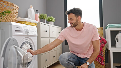 Young hispanic man smiling confident washing clothes at laundry room