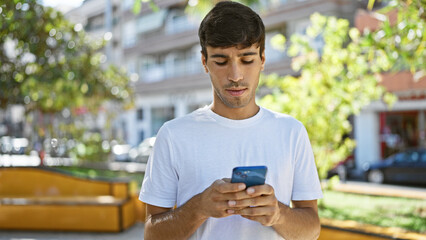 Cool looking young hispanic man, with serious expression, deeply engrossed in texting on smartphone...
