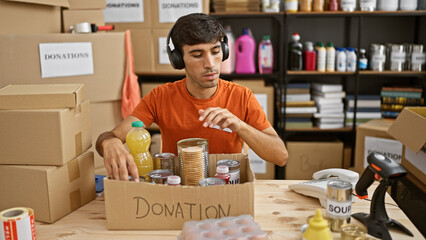 Warm-hearted young hispanic man volunteering at a charity center, confidently packing food into...