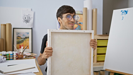 Smiling, confident young hispanic man draws passionately at art studio, a portrait of a handsome,...