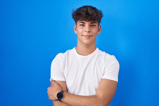 Hispanic teenager standing over blue background happy face smiling with crossed arms looking at the camera. positive person.