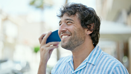 Young hispanic man listening to voice message smiling at street