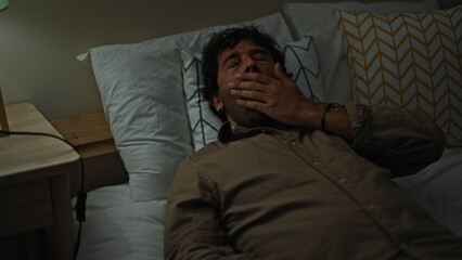 Fototapeta na wymiar Young hispanic man lying on bed tired yawning at bedroom