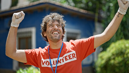 Young hispanic man activist wearing volunteer uniform doing winner gesture at park