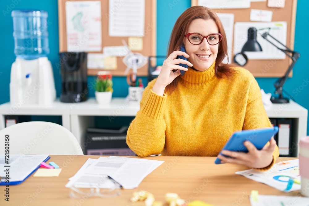 Wall mural young beautiful plus size woman business worker talking on smartphone using touchpad at office