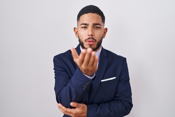 Young hispanic man wearing business suit and tie looking at the camera blowing a kiss with hand on air being lovely and sexy. love expression.