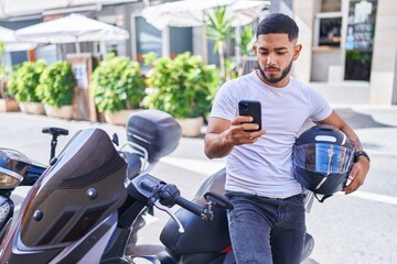 Young latin man using smartphone sitting on motorbike at street