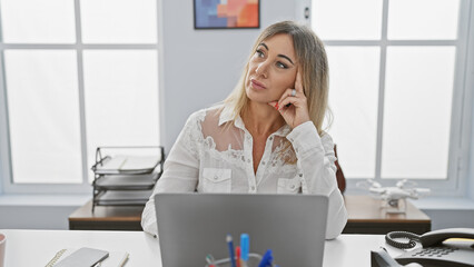 Pensive caucasian woman at office desk with laptop in a modern workspace