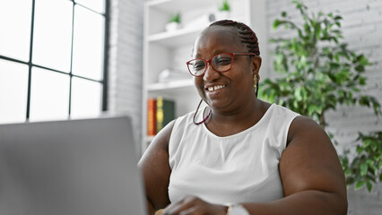 Confident african american woman boss, rocking braids and glasses, smiling as she's working online...
