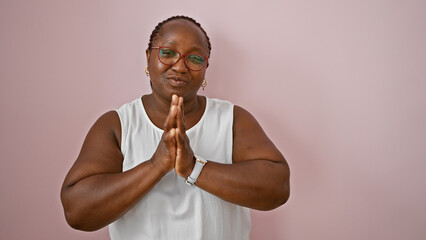 African american woman standing with hands together praying over isolated pink background