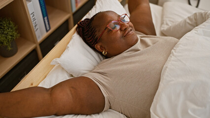Happy plus size african american woman stretching arms, waking up in comfortable bed at cozy...