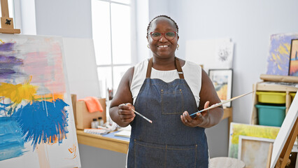 Cheerful african american woman artist, confidently holding paintbrush and palette, smiling bright...