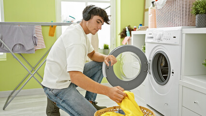 Handsome young hispanic teenager rocks out, engrossed in music, while tackling laundry chores in...