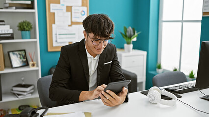 Young hispanic teenager grinning while doing business work, hands on touchpad at the office