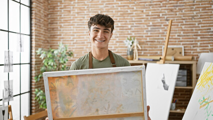 Smiling, confident young hispanic teenager artist merrily drawing on canvas at the cheerful art...