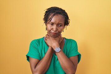 African woman with dreadlocks standing over yellow background shouting suffocate because painful...