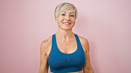 Mature woman with grey hair smiling in sportswear against a pink background