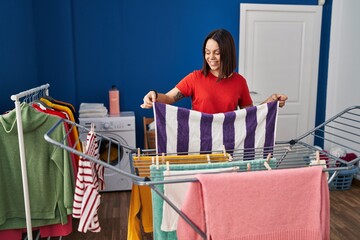 Young beautiful hispanic woman smiling confident hanging clothes on clothesline at laundry room