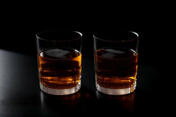 Two glasses of whiskey with ice on a black background, selective focus