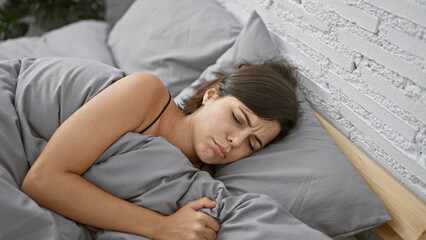 Exhausted yet beautiful young hispanic woman suffering insomnia, lying in the cozy comfort of her...
