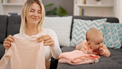 Mother and daughter holding baby clothes sitting together at home