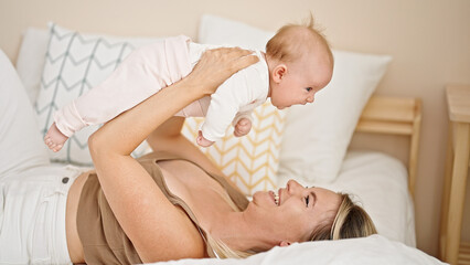 Mother and daughter lying on bed holding baby on air at bedroom