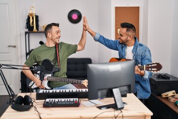 Two men musicians smiling confident high five with hands raised up at music studio