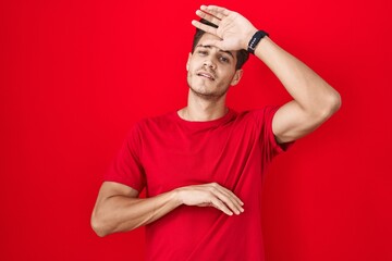 Fototapeta premium Young hispanic man standing over red background touching forehead for illness and fever, flu and cold, virus sick