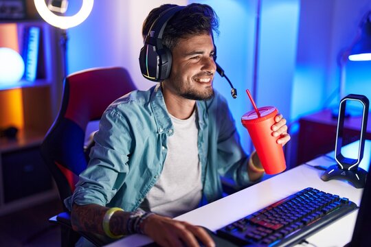 Young hispanic man streamer playing video game drinking beverage at gaming room - Powered by Adobe