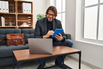 Middle age man psychologist using laptop and touchpad at psychology clinic