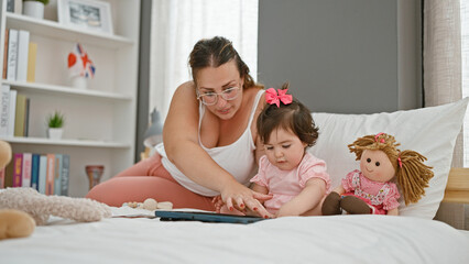 Cosy morning time, mother and daughter, comfortable in pyjamas, sitting together on bed, absorbed in touchpad technology, their beloved gadget, in a homely bedroom room