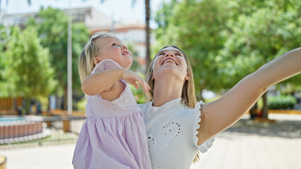 Confident mother holding her cheerful daughter in arms, standing at park looking up, enjoying...