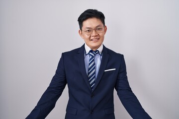 Young asian man wearing business suit and tie smiling cheerful with open arms as friendly welcome, positive and confident greetings