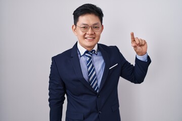 Young asian man wearing business suit and tie smiling and confident gesturing with hand doing small size sign with fingers looking and the camera. measure concept.