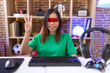 Middle age chinese woman wearing virtual reality glasses showing and pointing up with fingers...