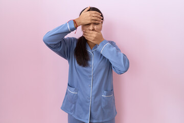 Young arab woman wearing blue pajama covering eyes and mouth with hands, surprised and shocked. hiding emotion