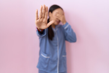 Young arab woman wearing blue pajama covering eyes with hands and doing stop gesture with sad and...