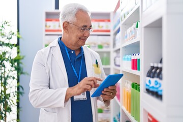 Middle age grey-haired man pharmacist using touchpad working at pharmacy