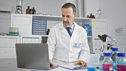 Serious middle-aged man with grey hair, a scientist deep in concentration, working on his laptop in a medical lab