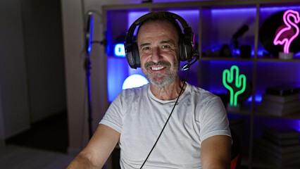 Smiling middle age man with grey hair commanding his stream! headphones on, gaming in his room till the wee hours!