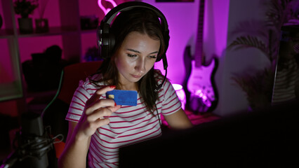 A young woman examines a credit card in a neon-lit gaming room at night