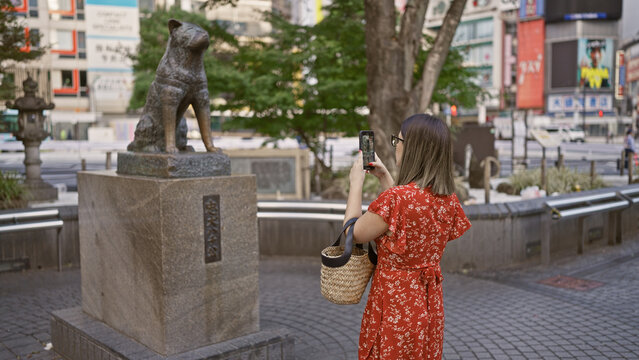 Beautiful hispanic woman in glasses taking memorable photos at hachiko statue in tokyo's urban cityscape