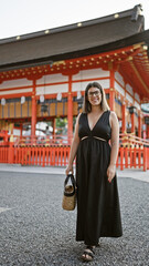 Captivating glimpse of a joyful confident hispanic woman, flashing a beaming smile in glasses, casually posing and walking towards the camera at the iconic fushimi inari-taisha in kyoto, japan.