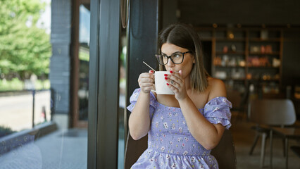 Relaxed beautiful hispanic woman in glasses, enjoying a hot cup of coffee at a cozy cafe table, taking a break from her busy morning indoors