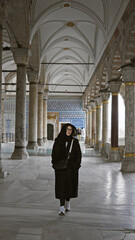 A brunette woman wearing glasses and a black coat stands in the historic topkapi palace in...