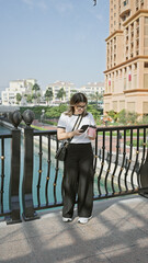 A young woman checks her phone in doha, showcasing modern architecture and the tranquil arabian skyline.