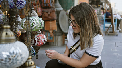 A young hispanic woman explores traditional lighting at souq waqif in doha, displaying culture and tourism. - obrazy, fototapety, plakaty
