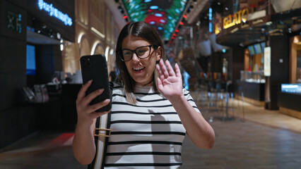 A smiling young hispanic woman waves while video calling on her smartphone inside a luxurious...