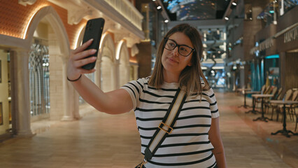 A young woman takes a selfie inside a modern luxury cruise ship with a sophisticated interior...